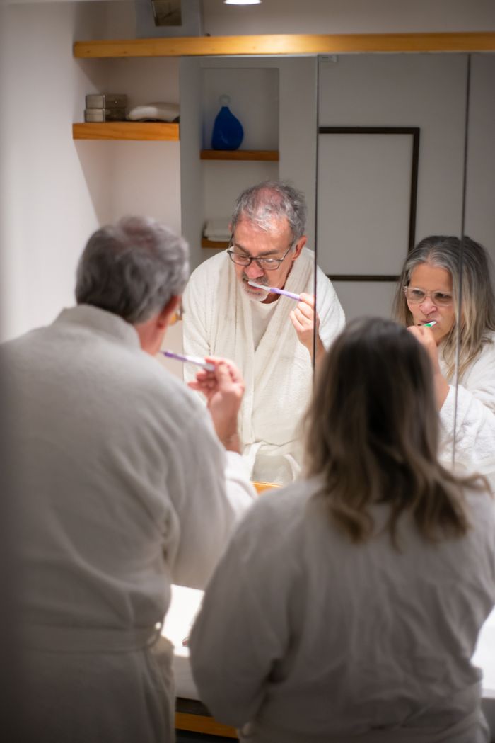 Senior couple wearing robes brushing their teeth together in a cozy bathroom.