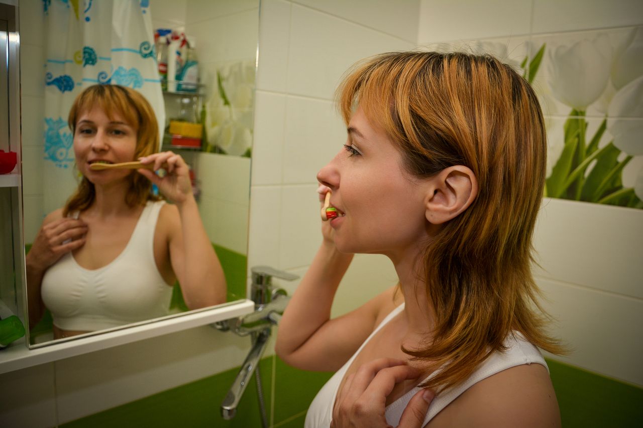 Redhead woman brushes teeth in bright bathroom, focusing on dental hygiene.